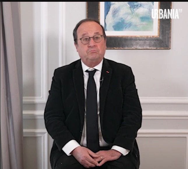 François Hollande assis devant un mur blanc sur lequel est accroché un cadre. Il fait une grimace