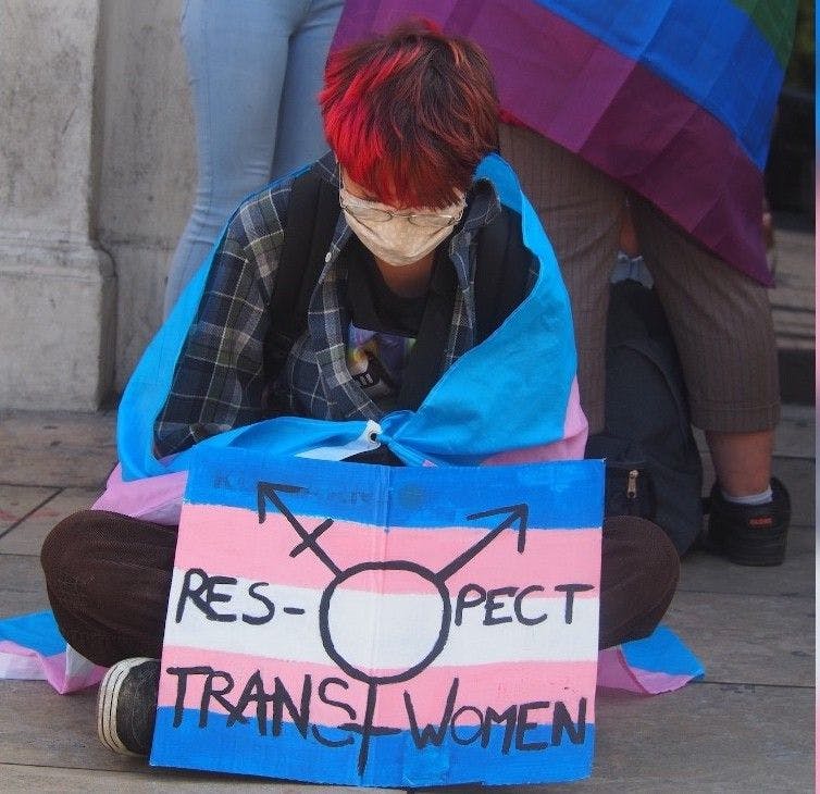 Une jeune femme avec une pancarte "Respect Trans Women" au couleur du drapeau trans