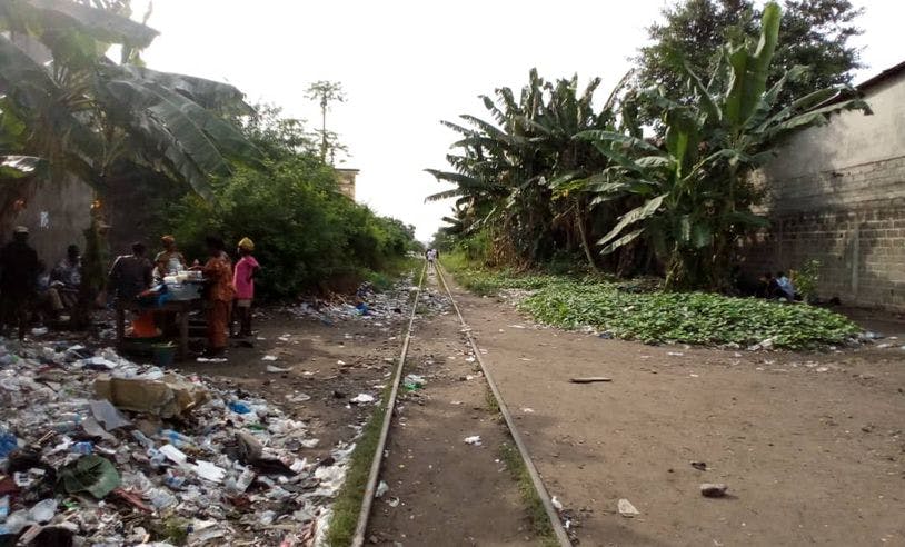 Une voie de chemin de fer, des détritus et des personnes sont entourés de palmiers. 