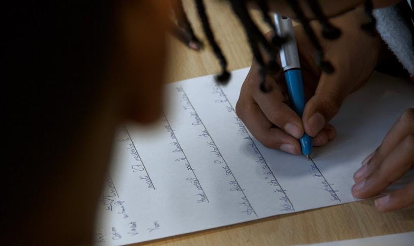 Un élève écrit sur une feuille de brouillon blanche